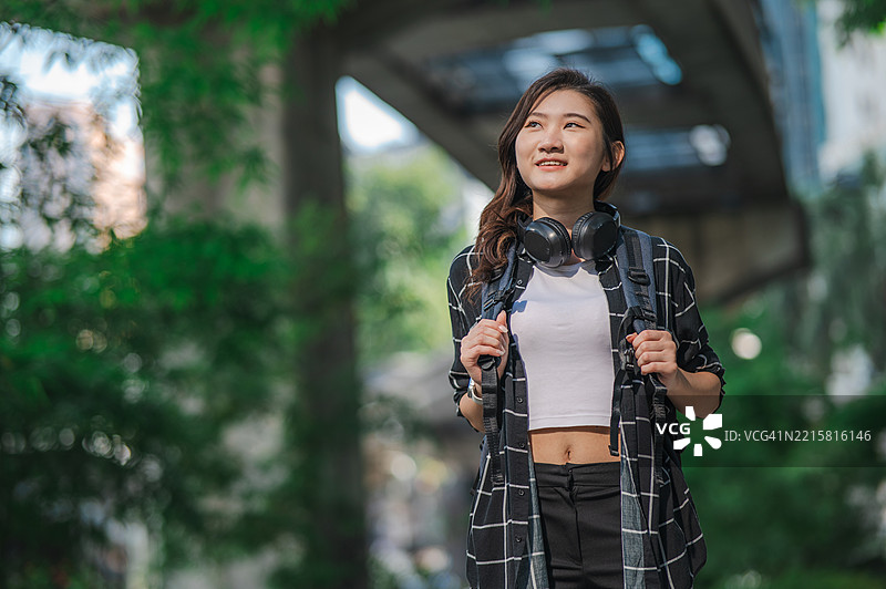 一位年轻的中国女性在户外公园背景下，手持智能手机，长发飘逸，肖像照片。图片素材
