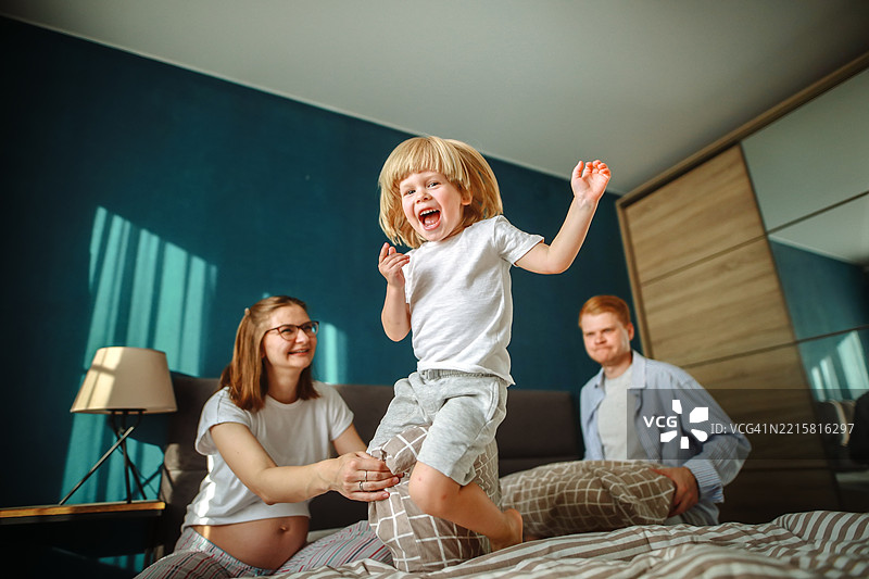 家庭幸福：金发孩子在父母身边兴奋地跳跃，洋溢着欢笑和温暖的传统家庭氛围。图片素材