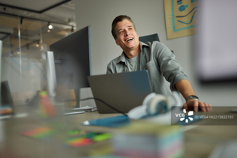 快乐的网页设计师在办公室使用笔记本电脑工作。图片素材