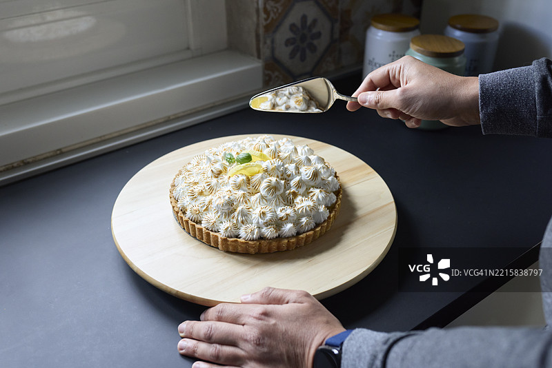 特写镜头：一名男子用蛋糕刀切自制的柠檬蛋白霜塔（Tarte au citron meringuée）图片素材
