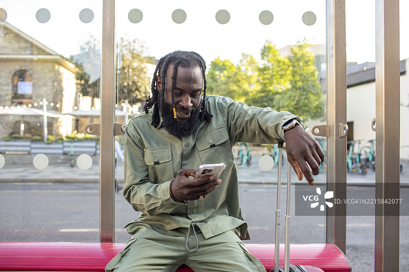 男子坐在公交车站，盯着智能手机。图片素材