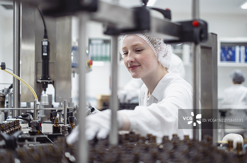 年轻实验室技术员在明亮的工业设施中操作自动包装生产线图片素材