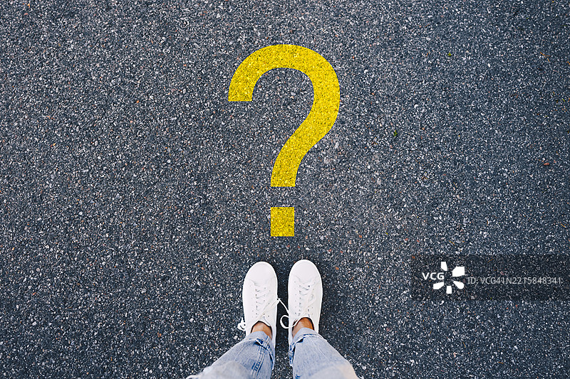 一个人站在涂在沥青上的黄色问号符号前图片素材