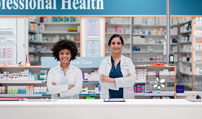 两位自信的女性药剂师在现代药房的柜台前微笑站立图片素材