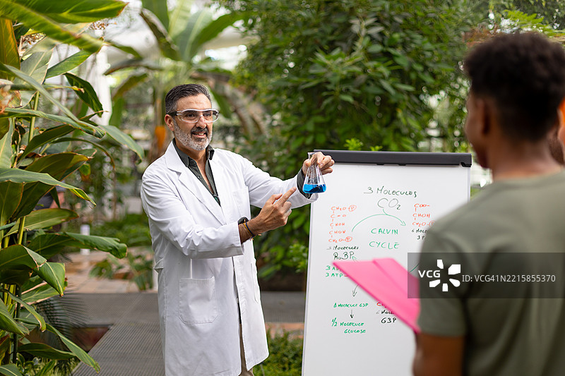 教授在温室里拿着烧杯向学生讲解化学知识图片素材