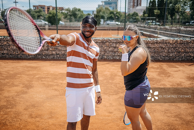 人们在阳光明媚的日子里在红土场上打网球并讨论战术图片素材