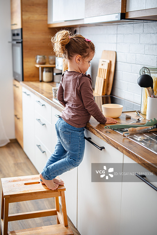 可爱的小女孩站在厨房的梯子上，试图模仿她的妈妈图片素材