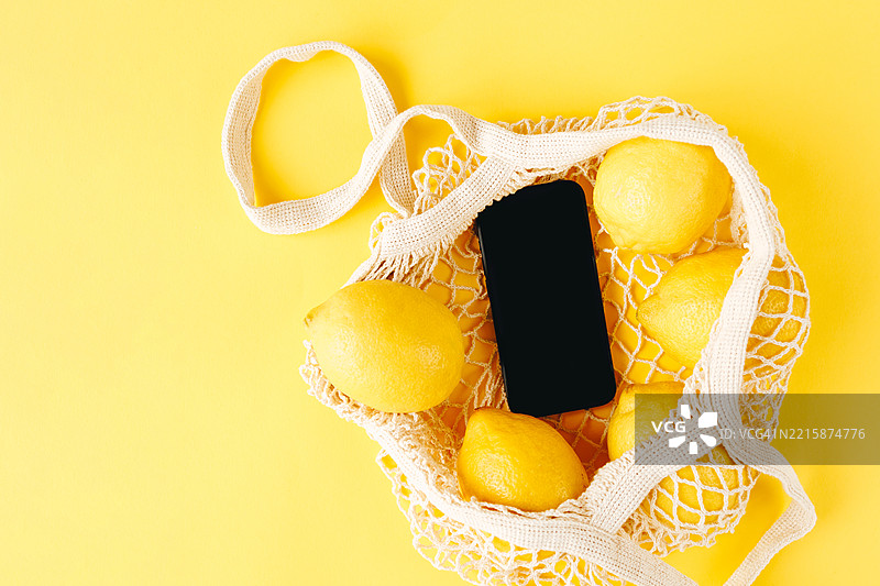 新鲜柠檬与智能手机放在可重复使用的购物袋中，背景为黄色图片素材