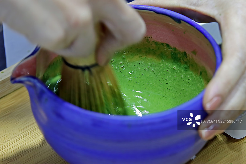 特写镜头：女性手持日本茶杯和茶筅，在桌上制作、搅拌和准备浓茶抹茶热饮。图片素材