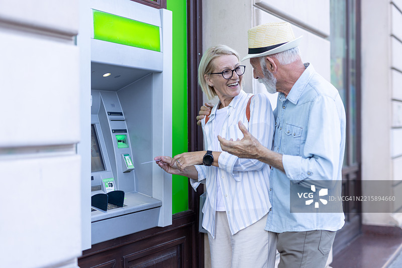 老年夫妇在户外的自动取款机前讨论财务事务图片素材
