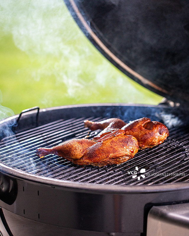 两块腌制的鸡肉在炭火烤架上冒烟。图片素材