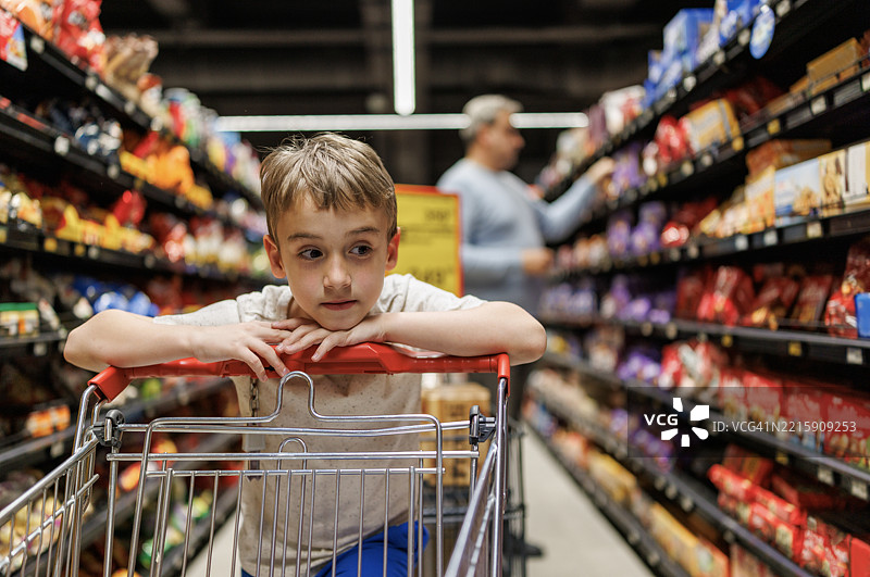 可爱的孩子在超市过道靠在购物车上图片素材