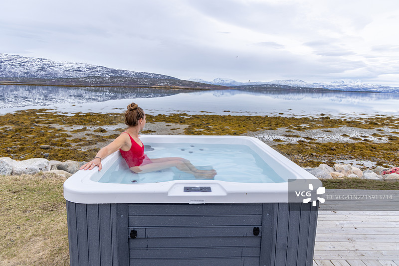 女人在热水浴缸中放松，俯瞰风景如画的雪山图片素材