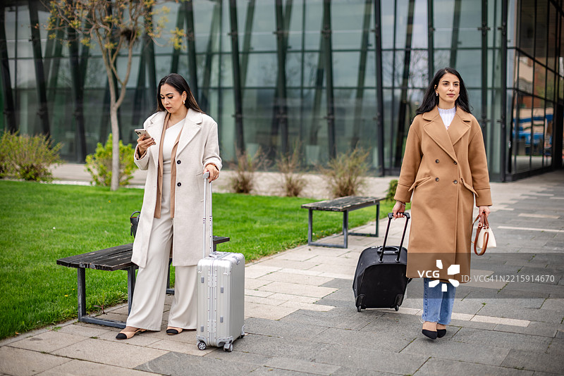 现代城市环境中，商务女性在办公大楼外携带行李匆匆而行图片素材