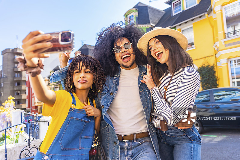 三位快乐的游客在智利瓦尔帕莱索的彩色房屋前用运动相机自拍图片素材