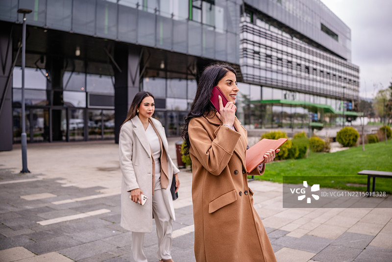 成功的女商人在现代企业办公楼外走动，同时在电话中讨论计划图片素材