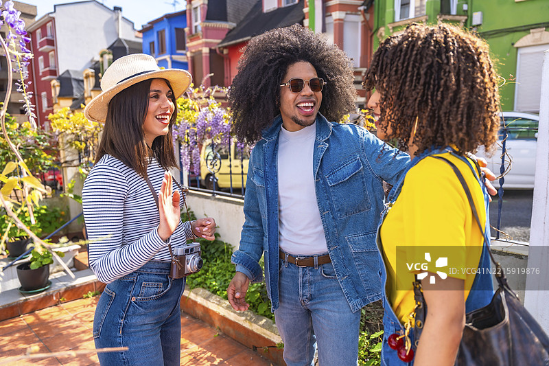 三位快乐的游客在色彩斑斓的住宅区互相问候，共同享受他们的假期。图片素材