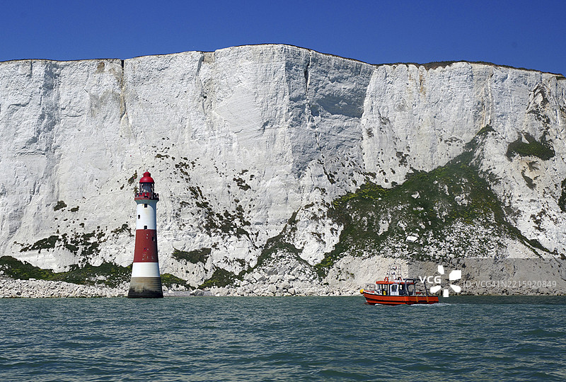 灯塔和小船在壮观悬崖背景前，游览，景点，海滩头灯塔，海滩头悬崖，英吉利海峡，伊斯特本，萨塞克斯，英格兰，英国图片素材