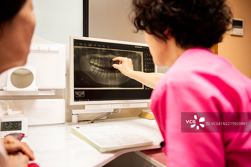 一位女牙医向一位年长女性患者展示她的牙齿X光片并为她解释。图片素材