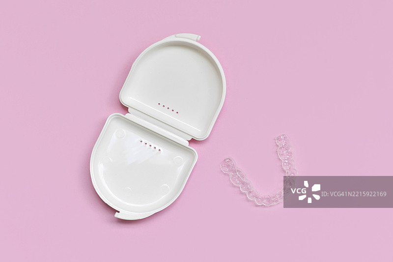 粉色背景上，定制透明牙齿咬合护具和下颌清晰矫正器的俯视图，配有白色储存盒。图片素材