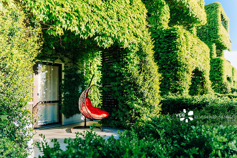 舒适的红色椅子旁边是一栋被常春藤和郁郁葱葱的绿植覆盖的住宅建筑图片素材
