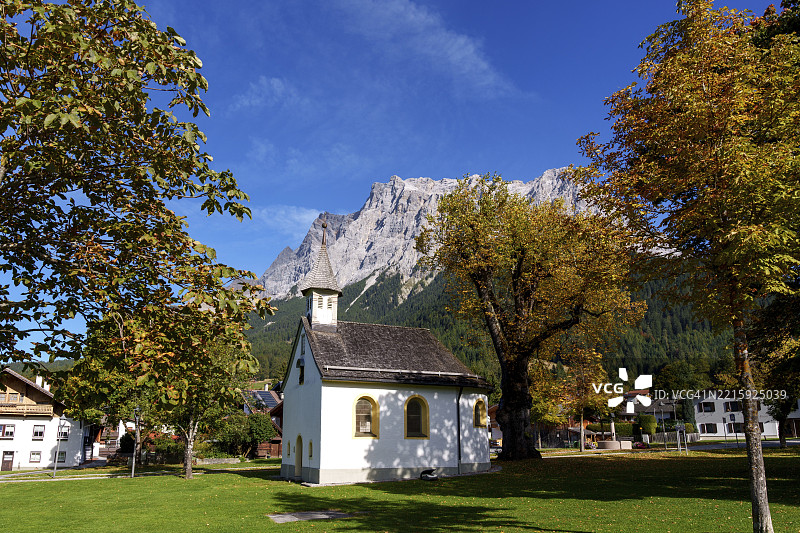 小教堂被秋天的树木环绕，背景是阿尔卑斯山脉，位于奥地利蒂罗尔州的厄尔瓦尔德，祖克峰。图片素材