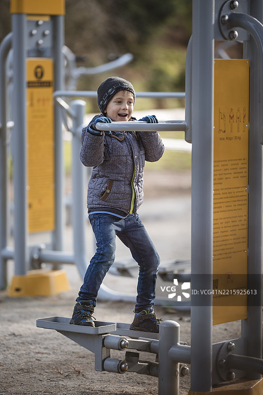 六岁男孩在户外健身器材上锻炼。该设备上有波兰语的使用说明。图片素材