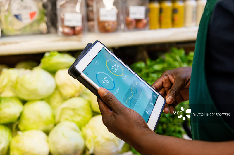 女销售员在超市检查新鲜蔬菜时，使用数字平板分析数据图片素材