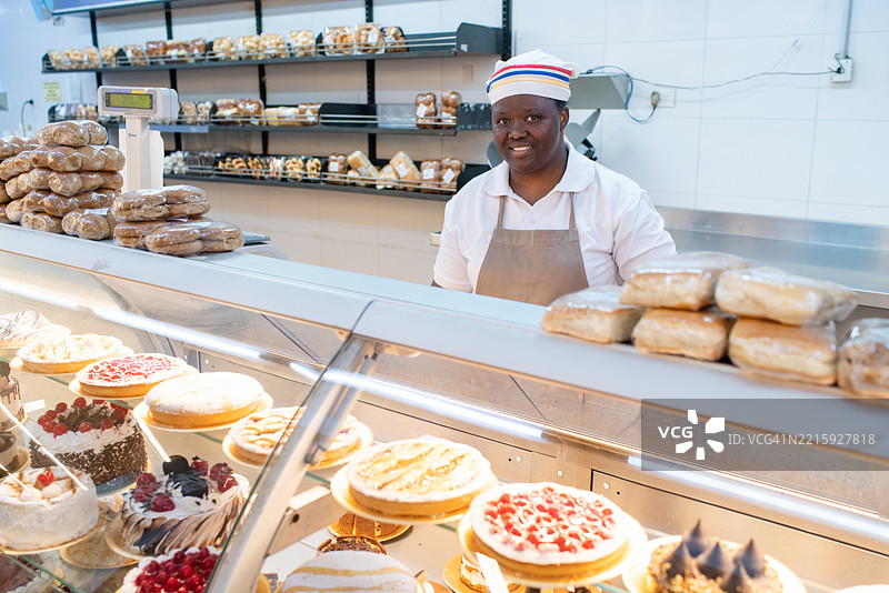 非洲女销售员站在商店的面包展示柜后面。图片素材