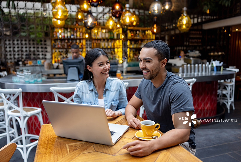 快乐的朋友们在餐厅里使用笔记本电脑并欢笑图片素材