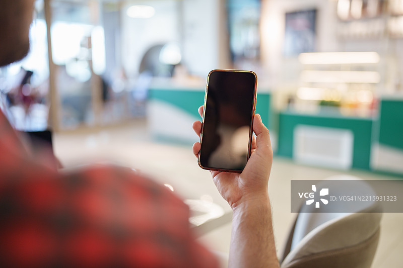 肩上视角的男子手持空白屏幕的智能手机图片素材