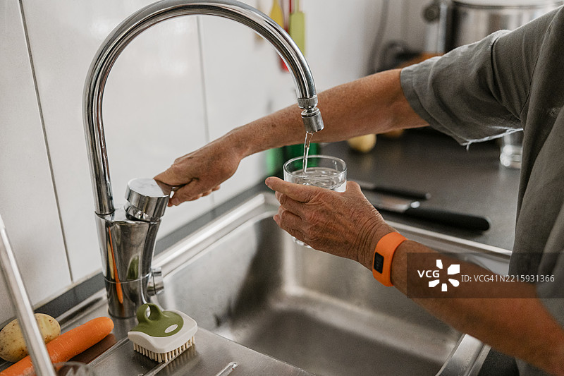 男人的手在厨房水槽的水龙头下给玻璃杯注水图片素材