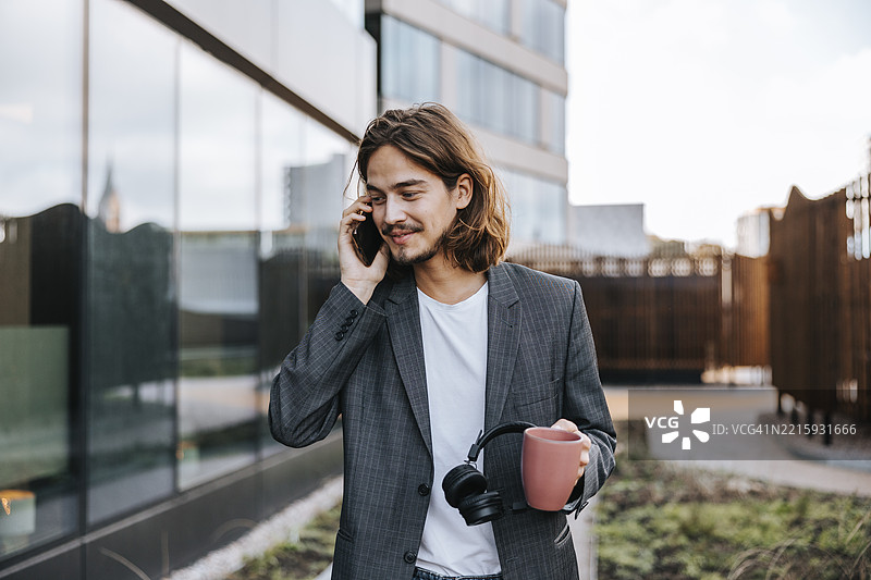 微笑的长发商人在办公楼外用智能手机通话图片素材