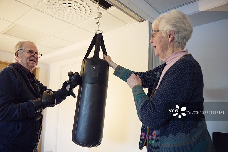 老年女性在康复中心帮助男性朋友击打沙袋训练图片素材