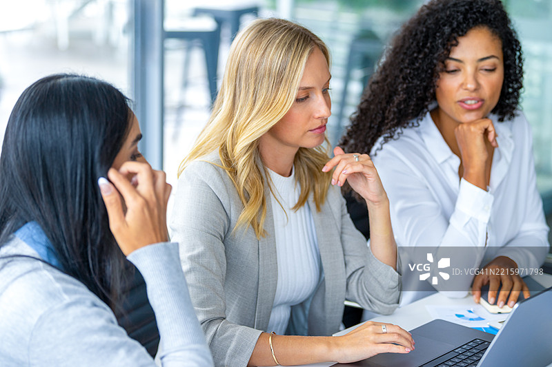 三位女性在会议室会面。桌子上有一台笔记本电脑。她们身后有一扇大窗户。图片素材