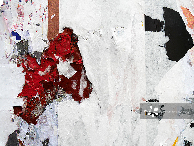 白色、红色和黑色的海报贴在墙上并撕裂的特写。粗糙的纹理。阳光。自然色彩。纽约州曼哈顿。图片素材