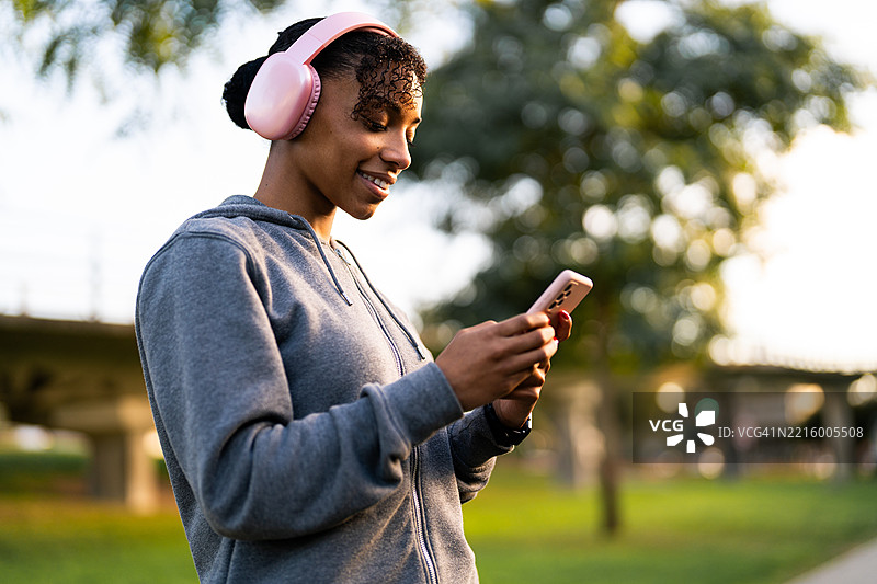 年轻女性在公园里戴着耳机听音乐，同时使用智能手机图片素材