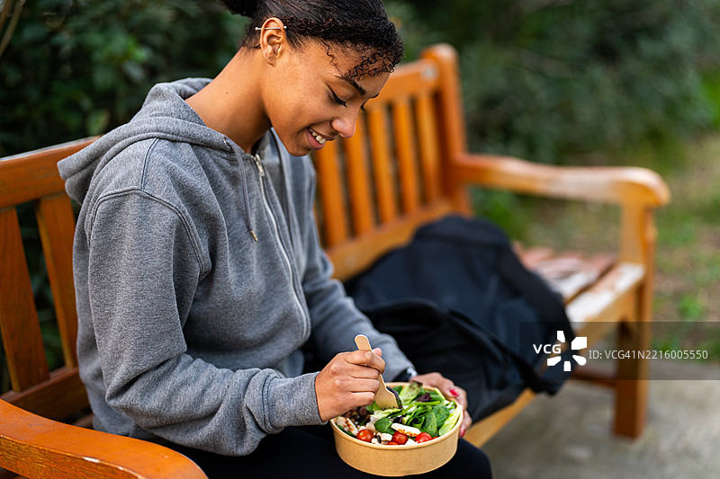 年轻运动员在公园长椅上训练后享用健康沙拉图片素材