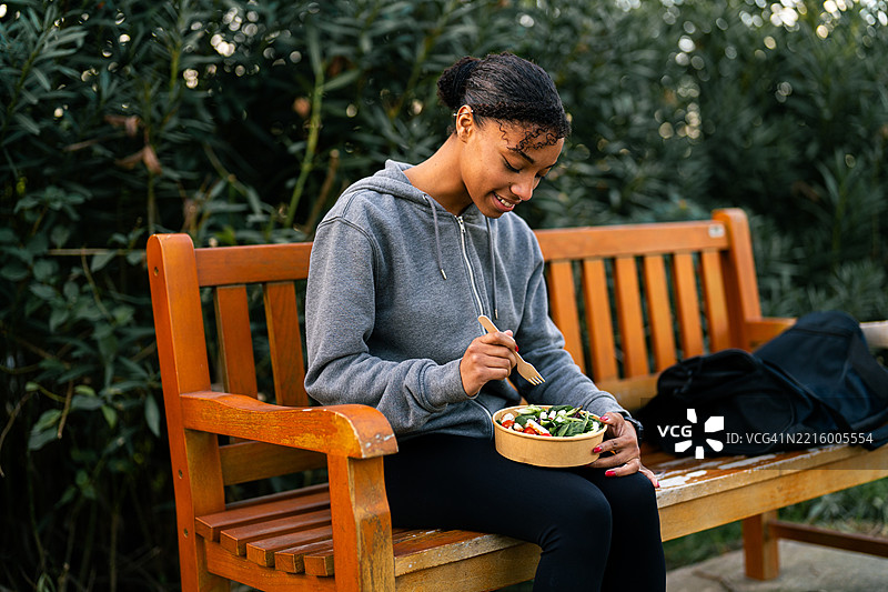 年轻运动员在公园长椅上训练后享用健康沙拉图片素材