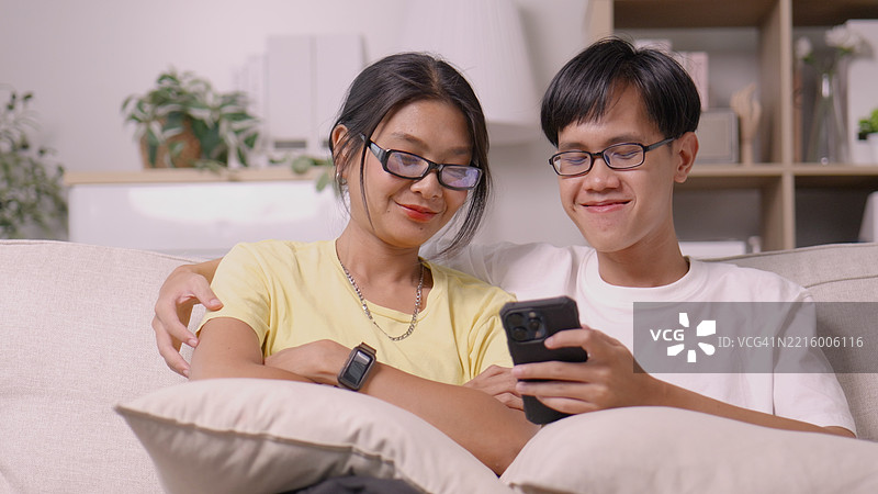 亚洲情侣在沙发上一起浏览手机，手牵手 – 温馨的关系时刻。4k图片素材