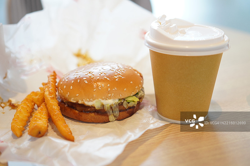 纸杯中的热咖啡，白纸上的汉堡猪肉配薯条，放在木桌上图片素材