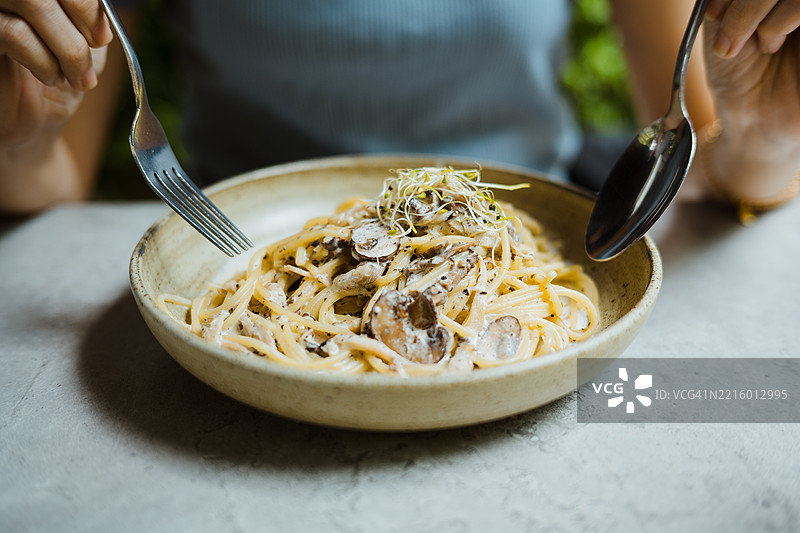 特写镜头，女人在桌子上用勺子和叉子吃卡邦尼意大利面。图片素材