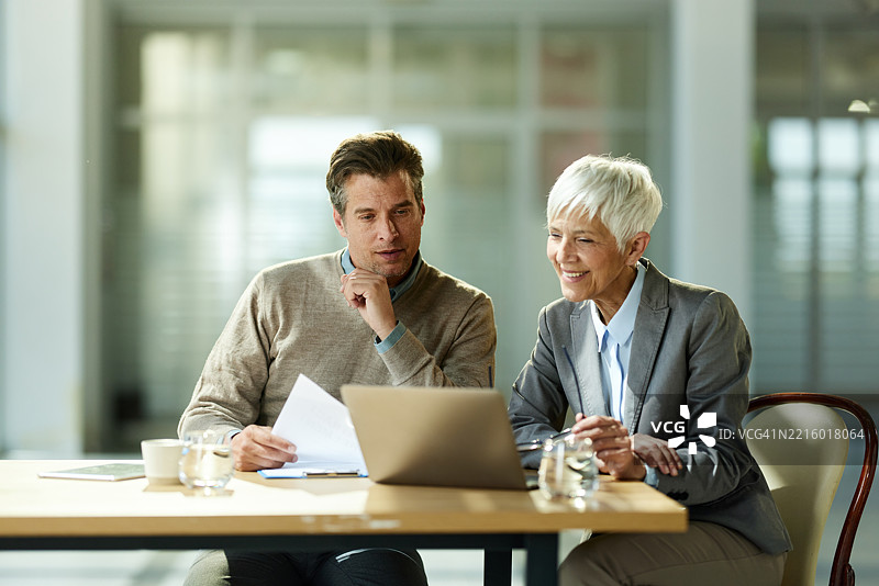 中年男子与他的保险代理人在办公室使用笔记本电脑。图片素材