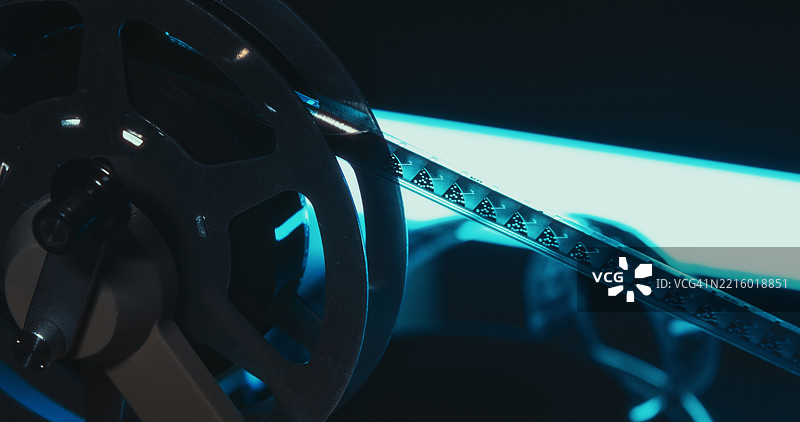 在蓝光下，16毫米胶卷带在机械卷轴中穿梭的特写镜头。图片素材