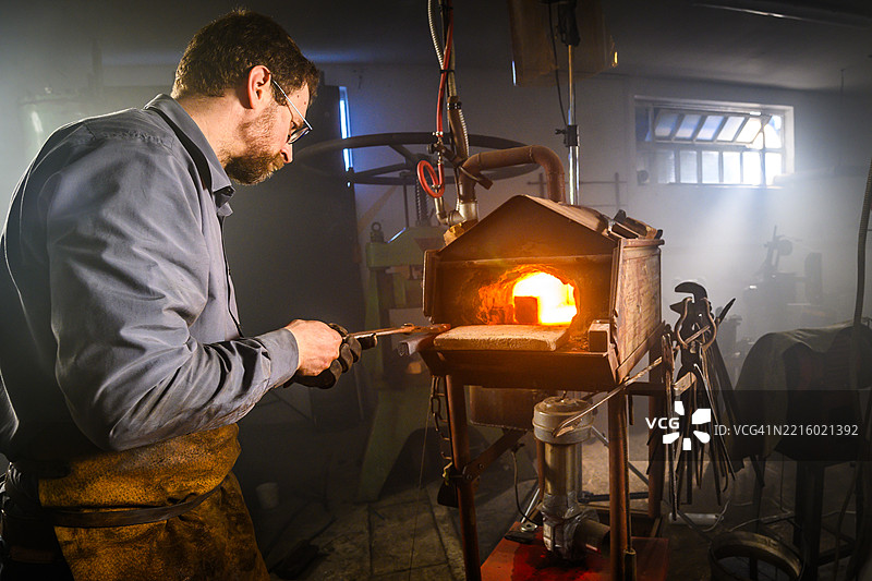专注的铁匠在明亮的锻造车间加热金属图片素材