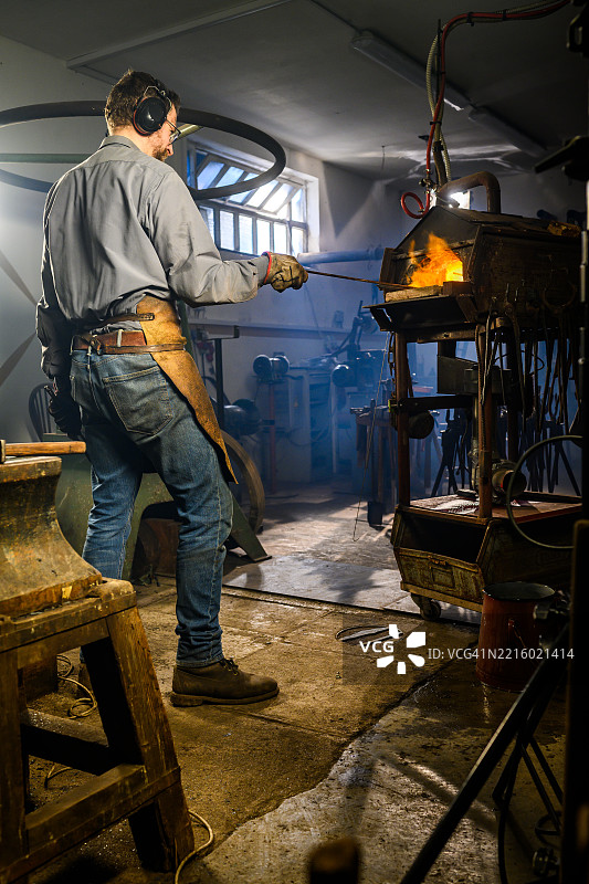 中年男性铁匠在乡村工作坊中使用熔炉图片素材