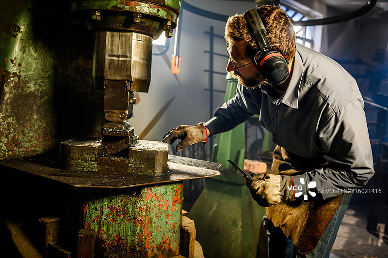 中年黑人铁匠在工业车间使用液压机图片素材