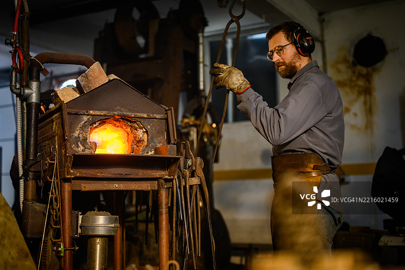 中年男性铁匠在传统室内工作坊中处理发热的金属图片素材