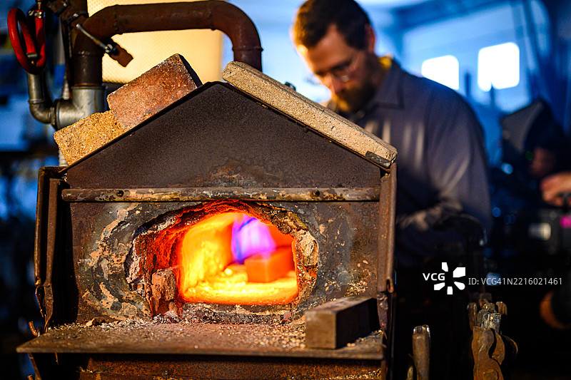 中年黑人铁匠在熔炉前工作，背景是发光的金属和乡村风格的工作坊图片素材