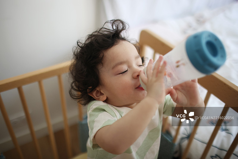 在家里的婴儿床上，18个月大的中国宝宝正在喝奶瓶。图片素材